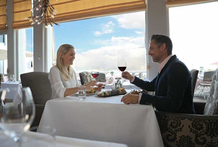 Paar genießt ein elegantes Dinner mit Wein im hellen Restaurant des ATLANTIC Grand Hotel Travemünde.
