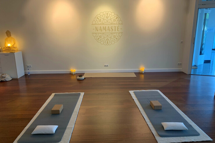 Yoga-Raum im ATLANTIC Grand Hotel Travemünde mit Matten, Kissen, Buddha-Statue und Kerzenlicht, "Namaste"-Wandmotiv.