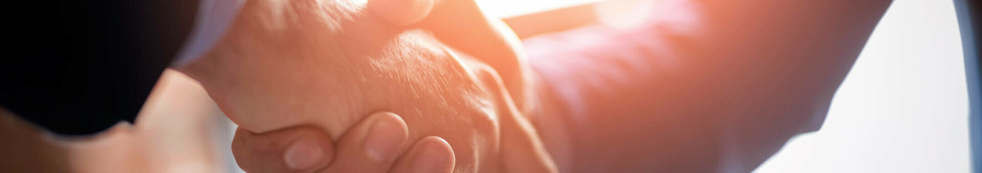 Ansprechpartner für Tagungen und Events im ATLANTIC Hotel Airport Bremen Zwei Personen in Anzügen geben sich die Hand bei Sonnenlicht.