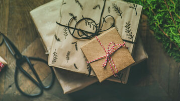 Geschenkverpackte Boxen mit Naturmotiven und rotem Band auf Holztisch, daneben eine Schere.