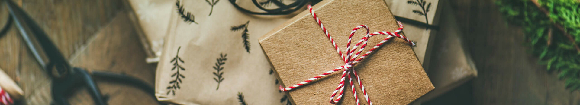 Geschenkverpackte Boxen mit Naturmotiven und rotem Band auf Holztisch, daneben eine Schere.