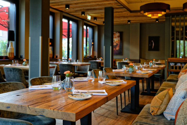 Restaurant CHALET im ATLANTIC Hotel Landgut Horn Bremen Gemütliches Restaurant mit Holztischen, gedeckt mit Gläsern und Tellern, warme Beleuchtung, große Fenster.