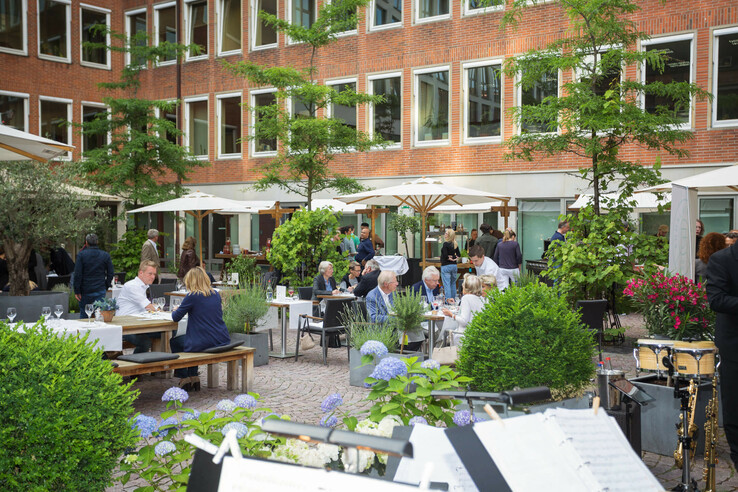 Lively hotel garden with guests at tables, surrounded by plants and parasols, at the ATLANTIC Grand Hotel Bremen.