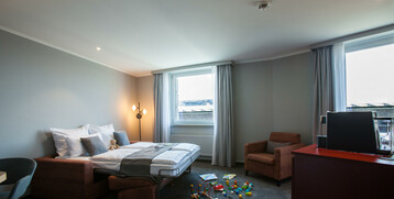 Helles Hotelzimmer mit Doppelbett, Sessel, Spielzeug auf dem Boden und großem Fenster im ATLANTIC Hotel Airport Bremen.