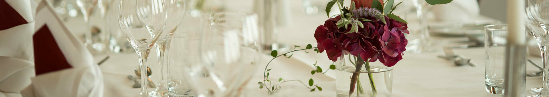 Elegant, festively laid table with white candles, wine glasses and red flower arrangements at the ATLANTIC Hotel Kiel.