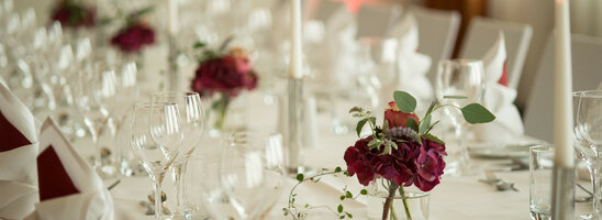 Elegant, festively laid table with white candles, wine glasses and red flower arrangements at the ATLANTIC Hotel Kiel.