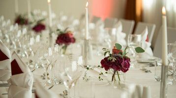 Elegant, festively laid table with white candles, wine glasses and red flower arrangements at the ATLANTIC Hotel Kiel.
