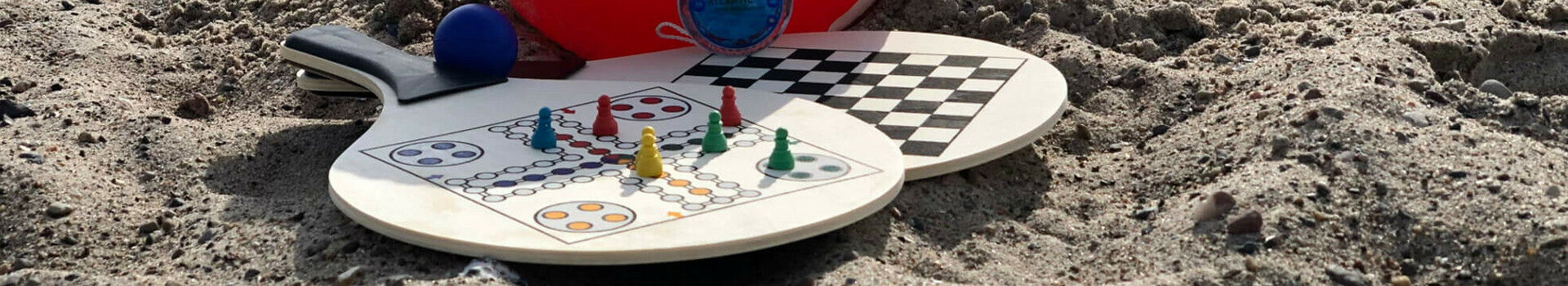 Strand mit rotem ATLANTIC-Ball, Brettspielen und Meer im Hintergrund, bei bewölktem Himmel.