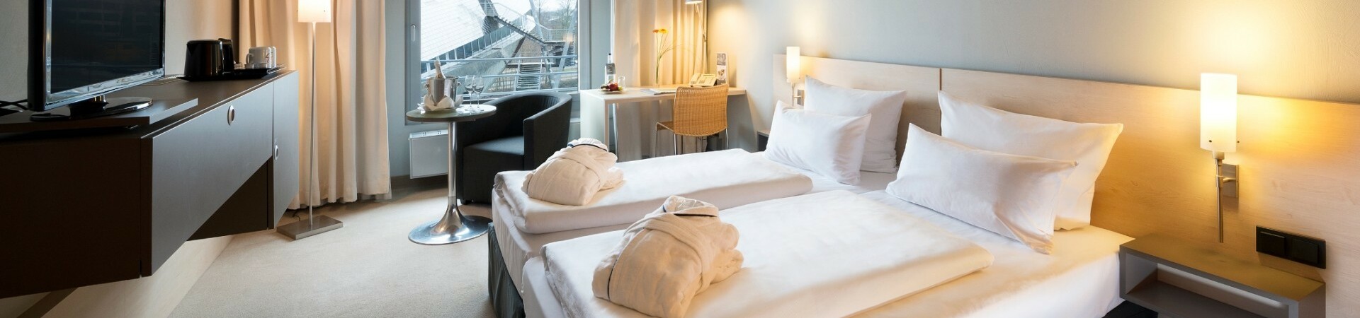 Modern hotel room with double bed, desk, armchair, TV and window with a view of futuristic architecture.