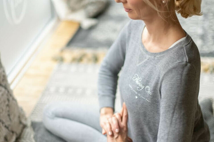 Frau in grauem Outfit meditiert auf Kissen am Fenster, entspannte Atmosphäre im ATLANTIC Grand Hotel Travemünde.