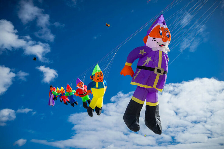 Bunte Drachen in Form von Figuren fliegen bei blauem Himmel.