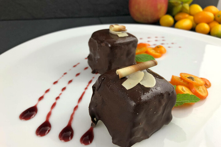 Chocolate dessert cubes with flaked almonds, fruit sauce and orange slices on a white plate, decorated with mint.