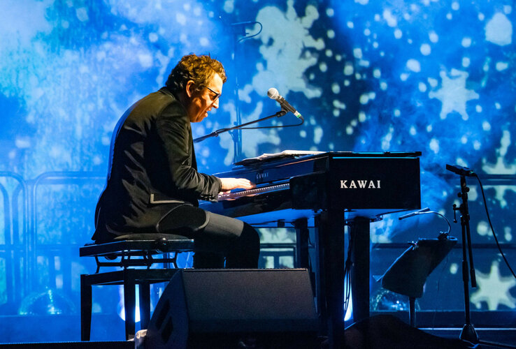 Ein Musiker spielt Klavier auf einer Bühne mit blauem, sternenartigem Hintergrund.