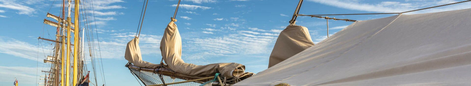 Sailing ships at the pier under a blue sky with clouds, ropes in the foreground.