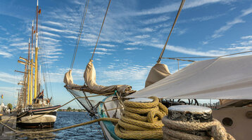 Sailing ships at the pier under a blue sky with clouds, ropes in the foreground.