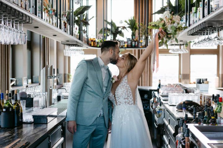Bride and groom kiss in a stylish hotel bar with modern details and plants at the ATLANTIC Hotel Heidelberg.