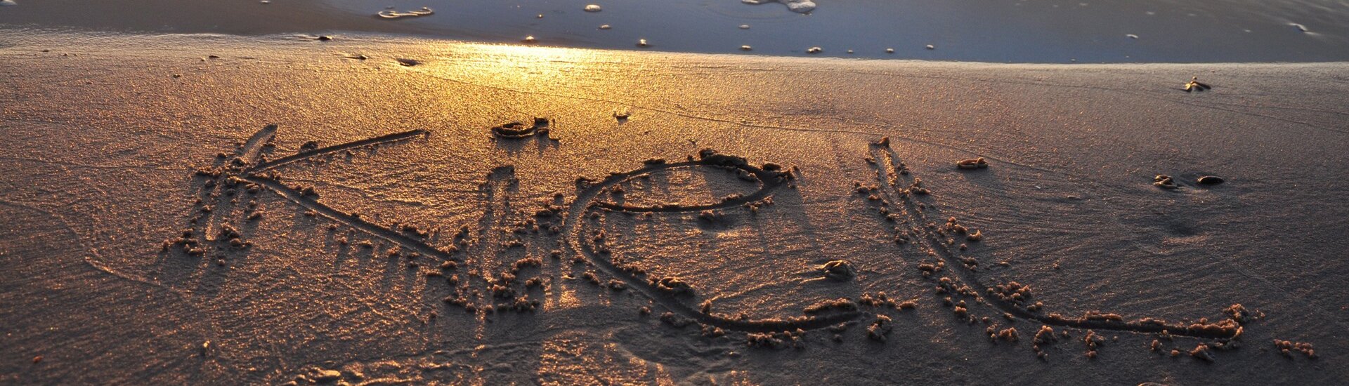 Kiel Schriftzug im Sand am Strand in der Nähe Kiels "Kiel" im Sand am Strand, beleuchtet vom warmen Licht eines Sonnenuntergangs.