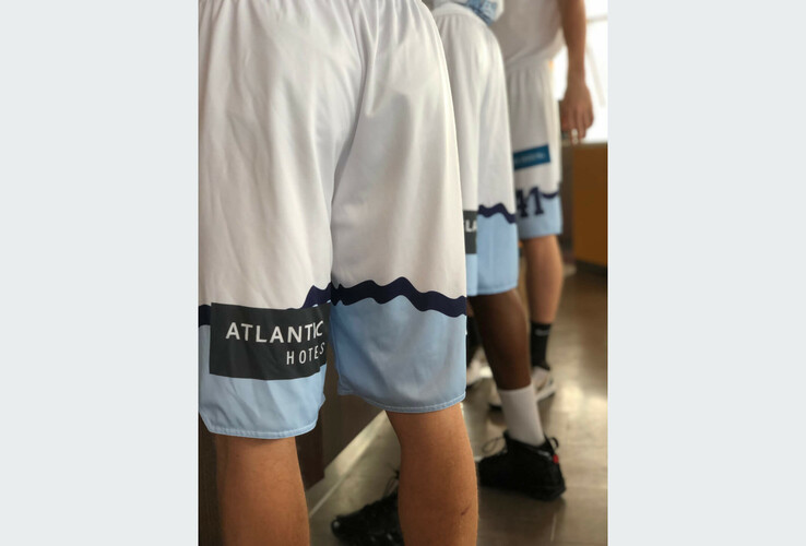 People in white shorts with the "ATLANTIC Hotels" logo stand in a row on a wooden floor.