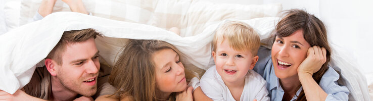Family offer ATLANTIC Hotel Universum  Family smiling happily under a comforter in a bright hotel room at the ATLANTIC Hotel Universum in Bremen.