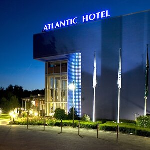 ATLANTIC Hotel Universum at night, illuminated facade, three flagpoles, well-kept entrance area.
