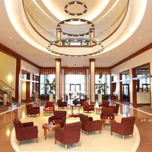 Hotelhalle des ATLANTIC Hotel Wilhelmshaven mit Sitzecke Elegante Hotellobby mit roten Sesseln, runden Tischen, modernen Kronleuchtern und Empfangsbereich rechts.