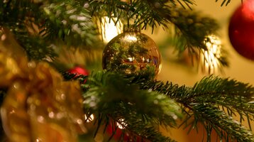 Nahaufnahme eines festlich geschmückten Weihnachtsbaums mit goldener Kugel und Lichtern.