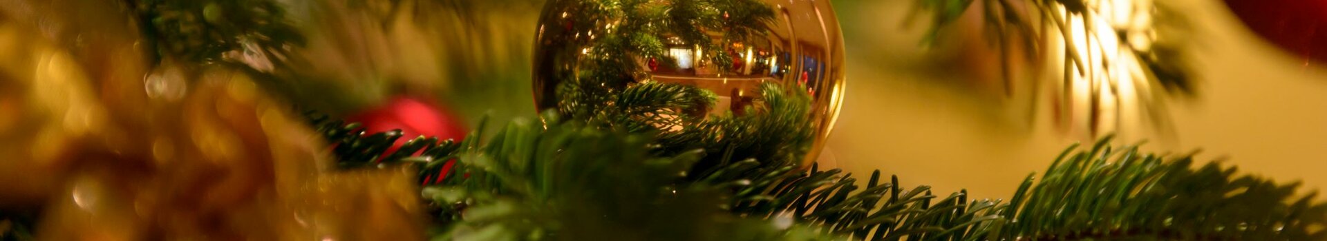 Nahaufnahme eines festlich geschmückten Weihnachtsbaums mit goldener Kugel und Lichtern.