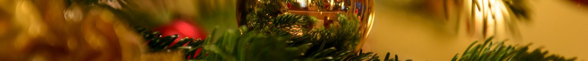 Nahaufnahme eines festlich geschmückten Weihnachtsbaums mit goldener Kugel und Lichtern.