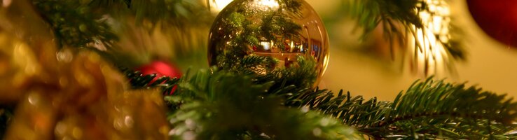 Nahaufnahme eines festlich geschmückten Weihnachtsbaums mit goldener Kugel und Lichtern.