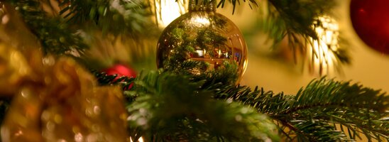 Nahaufnahme eines festlich geschmückten Weihnachtsbaums mit goldener Kugel und Lichtern.