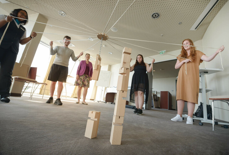 Group at team building in the ATLANTIC Hotel Bremerhaven, pulling ropes together to stack wooden blocks.