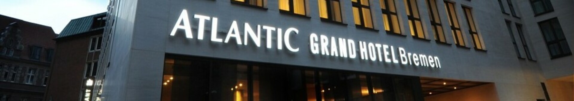 Modern hotel building at dusk, illuminated windows, "ATLANTIC Grand Hotel Bremen" lettering lights up.