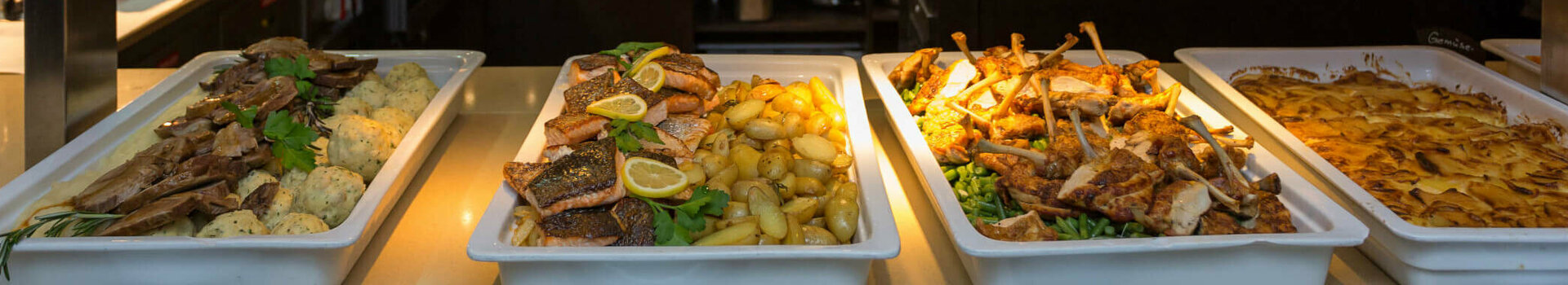 Buffet im ATLANTIC Grand Hotel Bremen mit verschiedenen Speisen in Schalen, darunter Fleisch, Kartoffeln und Gemüse.