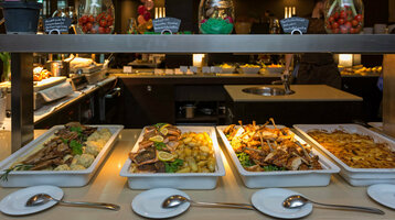 Buffet im ATLANTIC Grand Hotel Bremen mit verschiedenen Speisen in Schalen, darunter Fleisch, Kartoffeln und Gemüse.