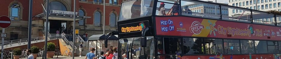 Ein roter Doppeldeckerbus für Stadtrundfahrten steht vor dem historischen Bahnhofsgebäude in Kiel.