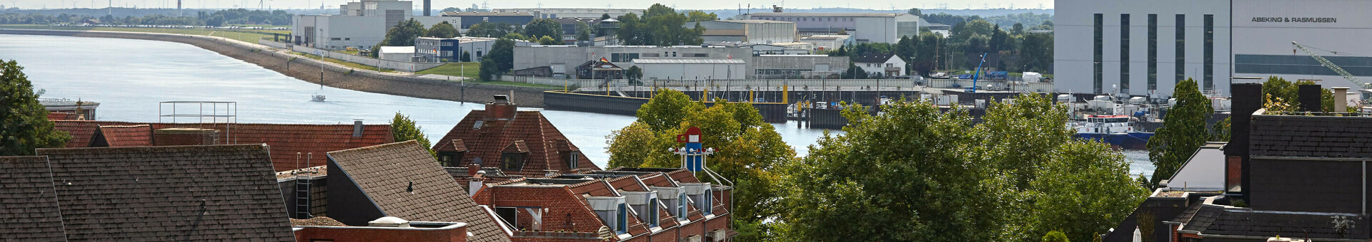 Blick vom ATLANTIC Hotel Vegesack auf die Weser, mit Werft und Windrad im Hintergrund unter bewölktem Himmel.