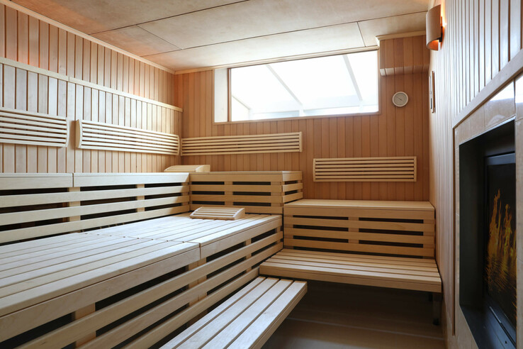 Helle Sauna im ATLANTIC Grand Hotel Travemünde mit Holzverkleidung und Sitzbänken, Fenster oben, Kamin an der Wand.