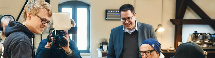 Der Kaffee von Münster Personen bei einer Kaffeeverkostung an einem Holztisch, Fotograf im Hintergrund.