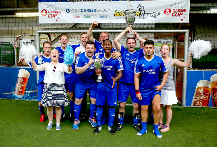 Ein jubelndes Fußballteam des ATLANTIC Hotels mit Pokalen, umgeben von fröhlichen Unterstützern.