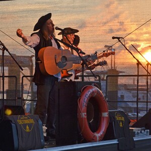 Live band on stage at sunset, musicians in maritime clothing, the harbor of Vegesack in the background.