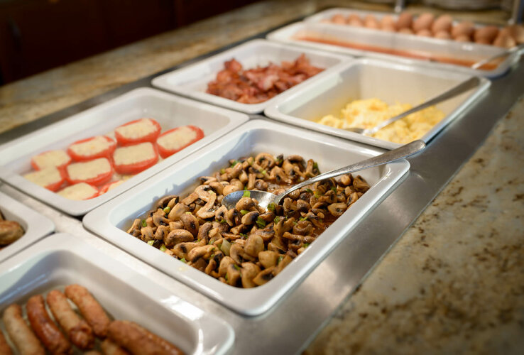 Buffet mit Pilzen, Würstchen, Eiern und Tomaten auf einem Frühstückstisch.