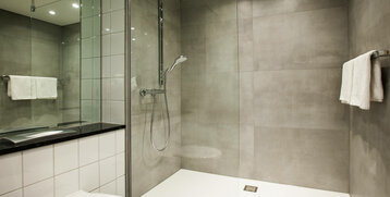 Modernes Badezimmer mit ebenerdiger Dusche, Handtuchhalter und grauen Fliesen im ATLANTIC Hotel Airport Bremen.