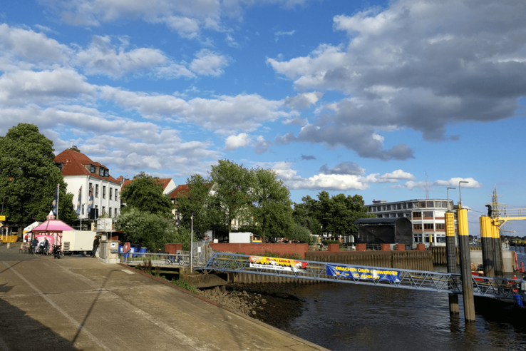 Blick auf die Weserpromenade in Vegesack mit Gebäuden, Bäumen und blauem Himmel.