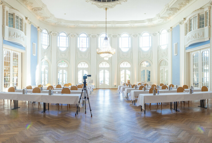 Heller, eleganter Ballsaal im ATLANTIC Grand Hotel Travemünde mit Tischen, Stühlen und Kronleuchter.
