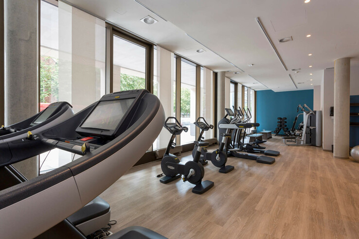 Heller Fitnessraum im ATLANTIC Grand Hotel Bremen mit Laufbändern, Fahrradergometern und Kraftgeräten vor großen Fenstern.