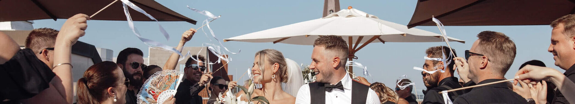 ATLANTIC Grand Hotel Bremen Hochzeit auf der Grand Terrace Hochzeitspaar verlässt strahlend eine festliche Zeremonie im Freien, umgeben von jubelnden Gästen mit Bändern.