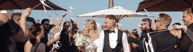 ATLANTIC Grand Hotel Bremen Hochzeit auf der Grand Terrace Hochzeitspaar verlässt strahlend eine festliche Zeremonie im Freien, umgeben von jubelnden Gästen mit Bändern.