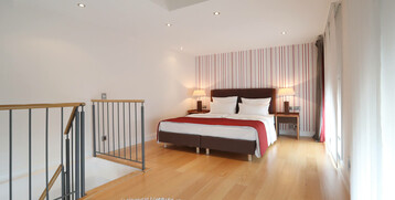 Modernes Hotelzimmer mit Doppelbett, Holzfußboden, gestreifter Tapete und zwei Nachttischlampen im ATLANTIC Grand Hotel.