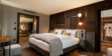 Modernes Hotelzimmer mit Doppelbett, Holzwänden, und Blick in einen Wohnbereich. Elegantes Design mit warmen Farben.