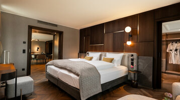 ATLANTIC Hotel Heidelberg Grand Suite Modernes Hotelzimmer mit Doppelbett, Holzwänden, und Blick in einen Wohnbereich. Elegantes Design mit warmen Farben.